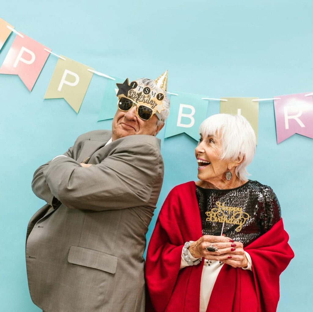 Elderly couple in festive attire celebrating a joyful birthday with laughter.